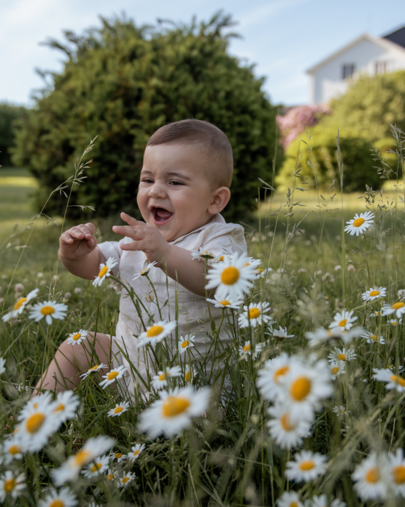 Lille dreng sidder i blomstereng og griner